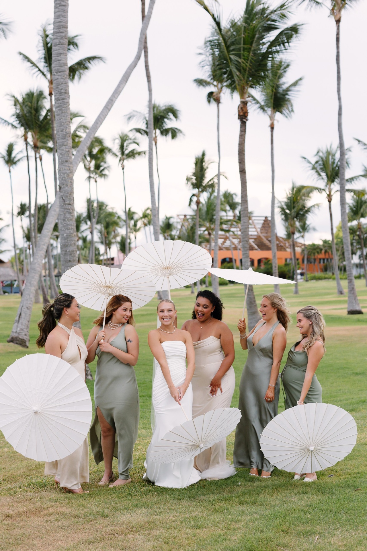 Bride and bridesmaids walking with ivory parasols across the resort lawn at a Dominican Republic destination wedding