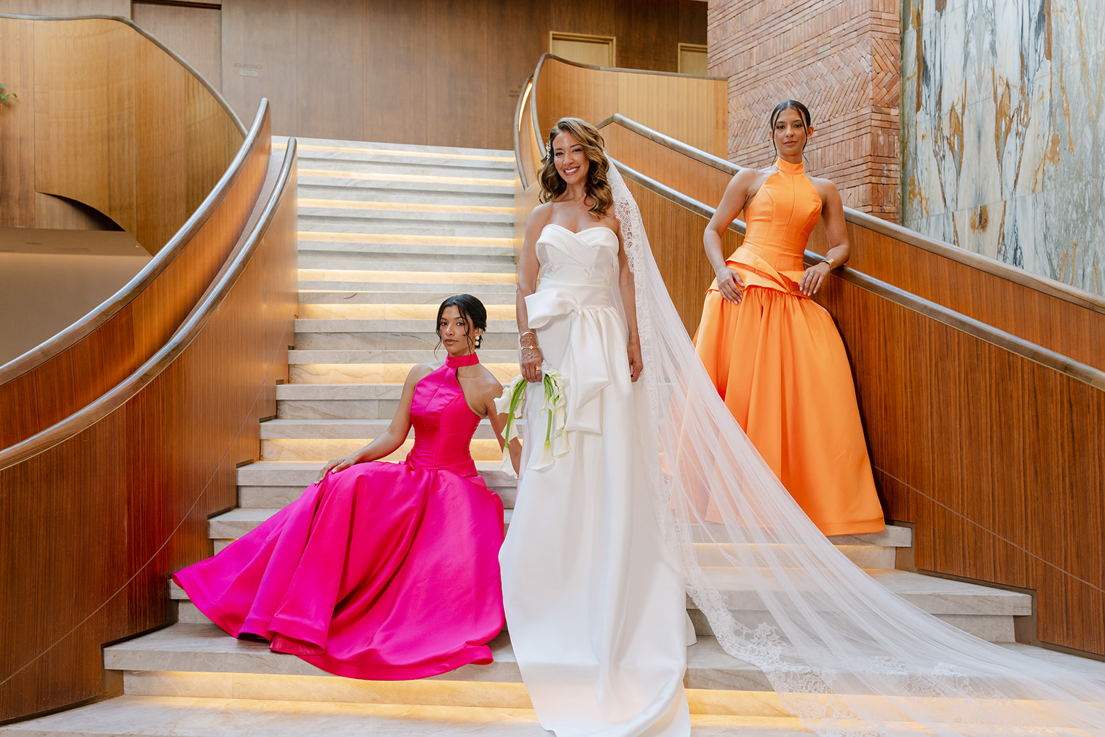 Yevette in her wedding gown with her daughters in fuchsia and orange gowns on the St. Regis staircase